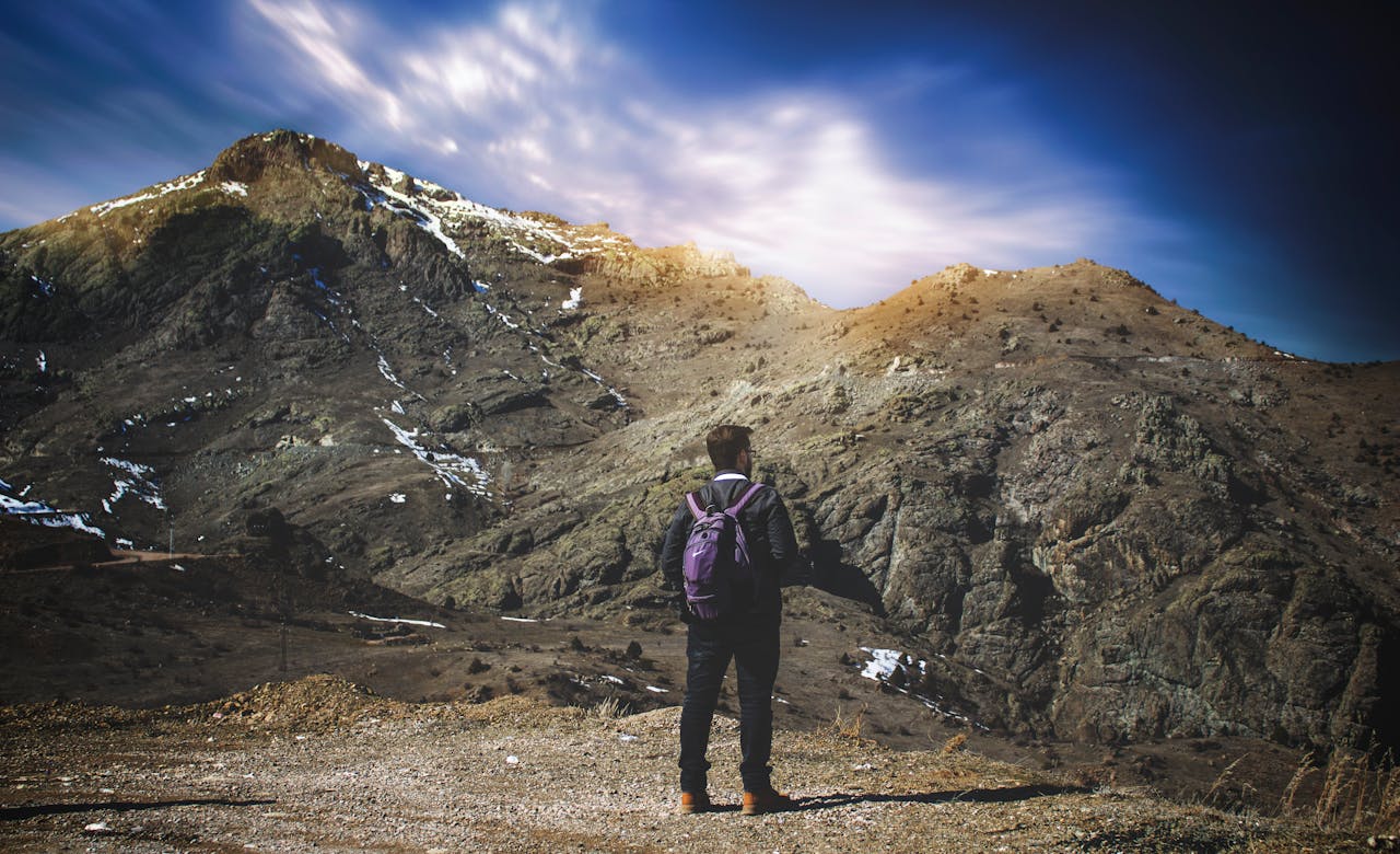 A lone hiker with a purple backpack explores a rugged mountain terrain under a vivid sky.